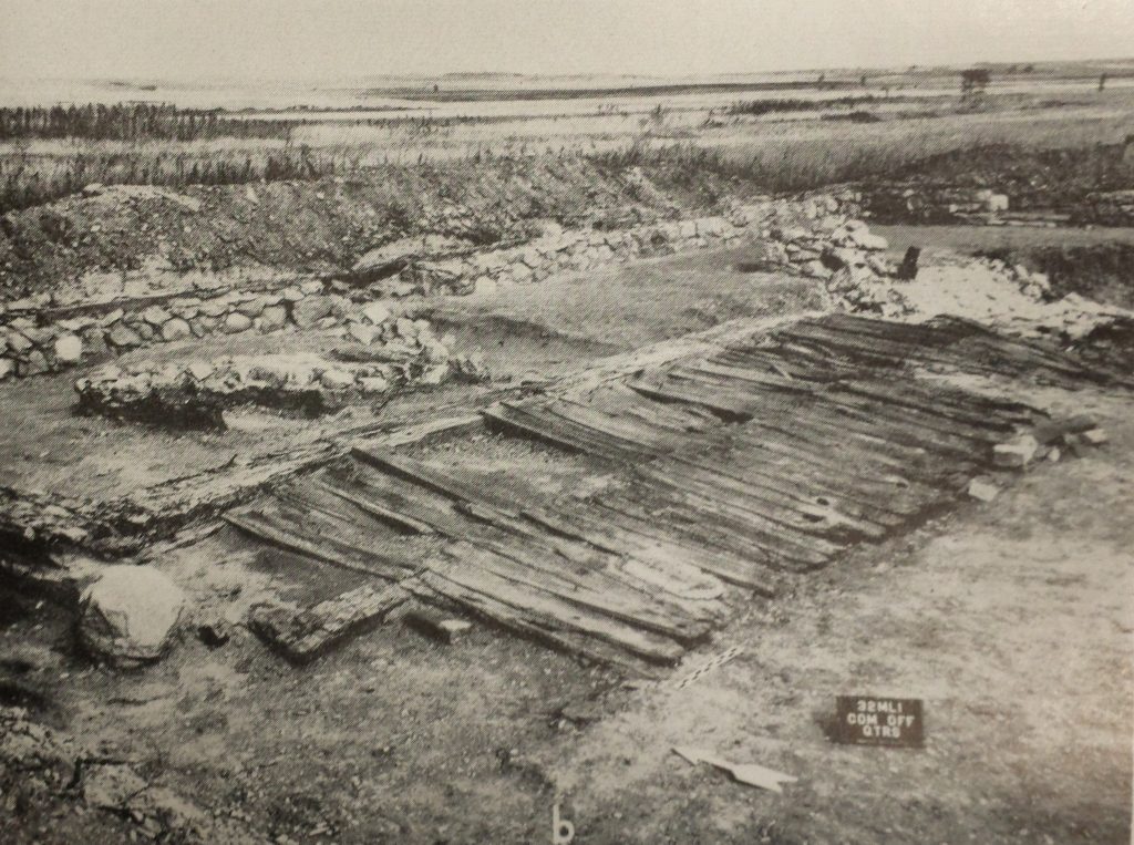 Black-and-white photo of excavation area, showing wooden planks in situ.