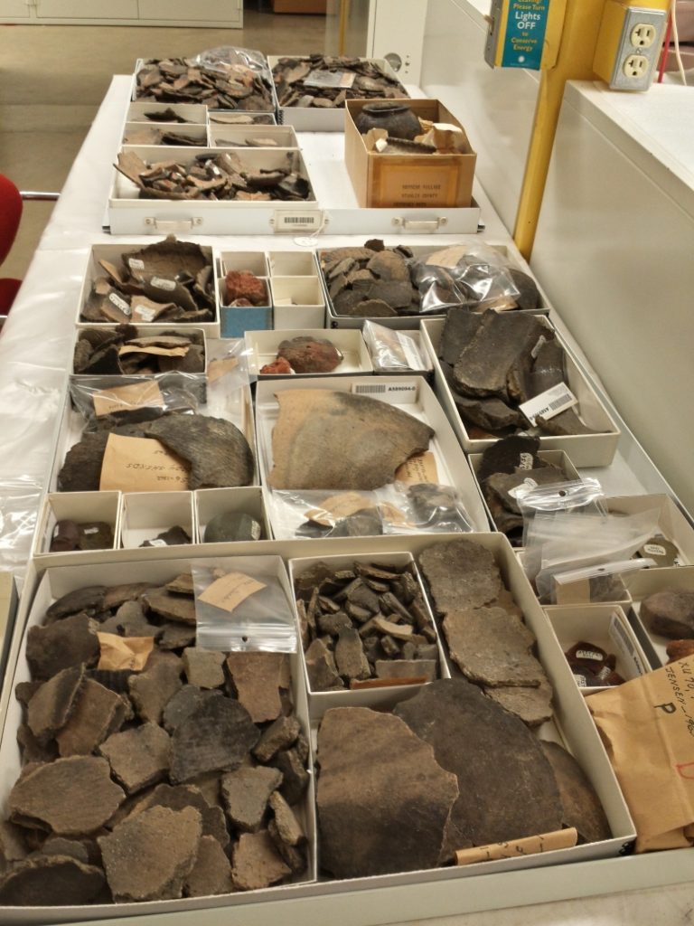 Two metal drawers sitting on a long table. Each is filled with cardboard artifact boxes full of ceramic sherds of various sizes.