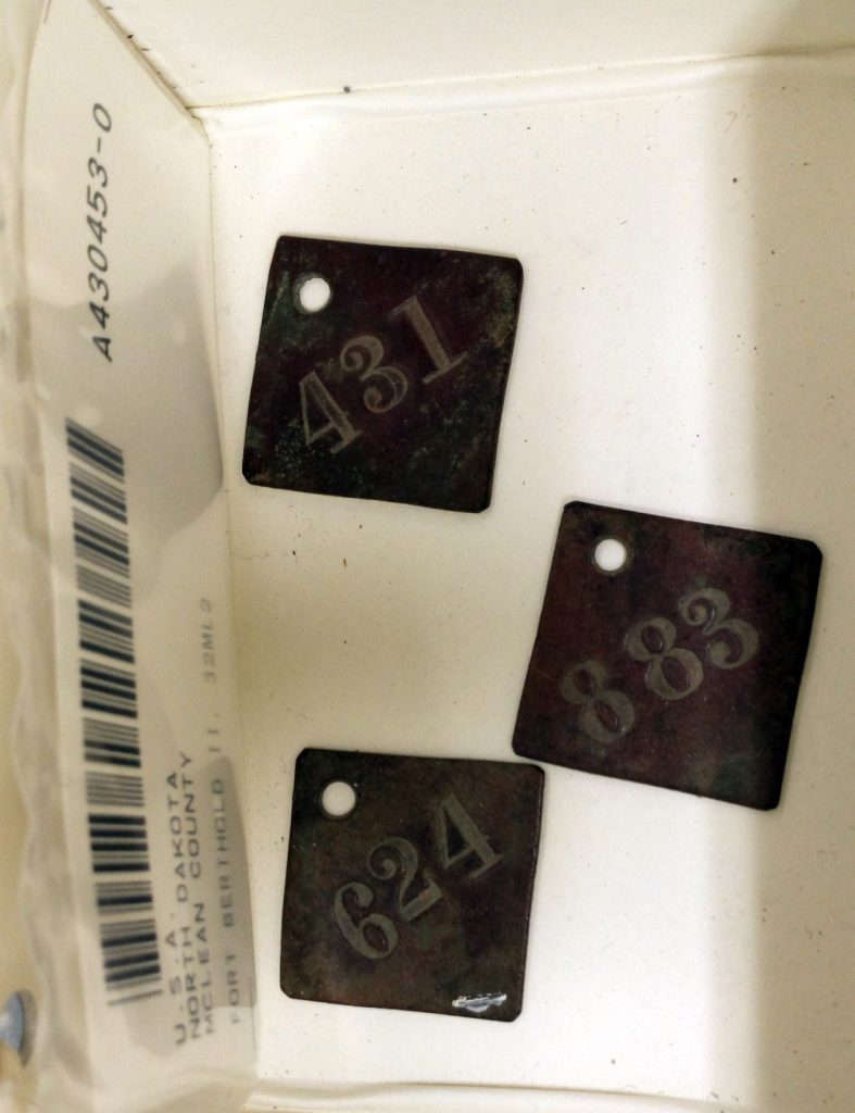 Three diamond-shaped metal tags, each with a three-digit number stamped on it and a hole in one of the corners. The numbers are 431, 883, and 624.