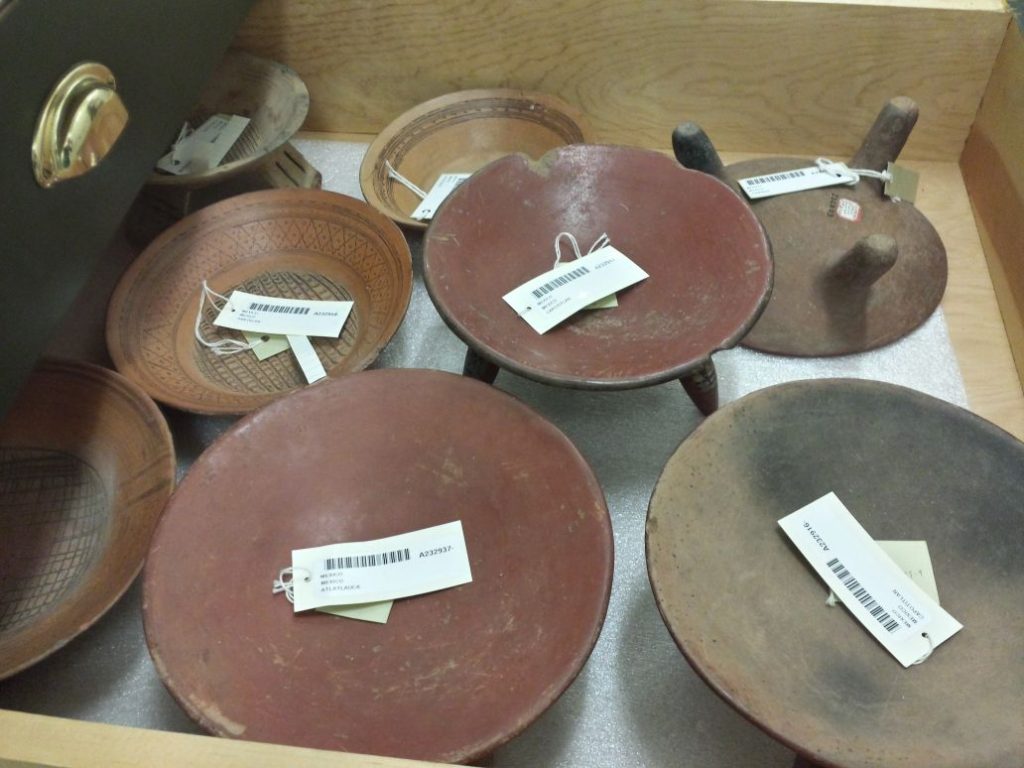 A wooden drawer with whole ceramic vessels in shades of red and orange.