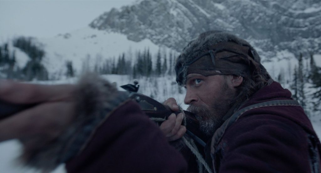 Still from The Revenant. Tom Hardy as John Fitzgerald, aiming his rifle in a snowy landscape.