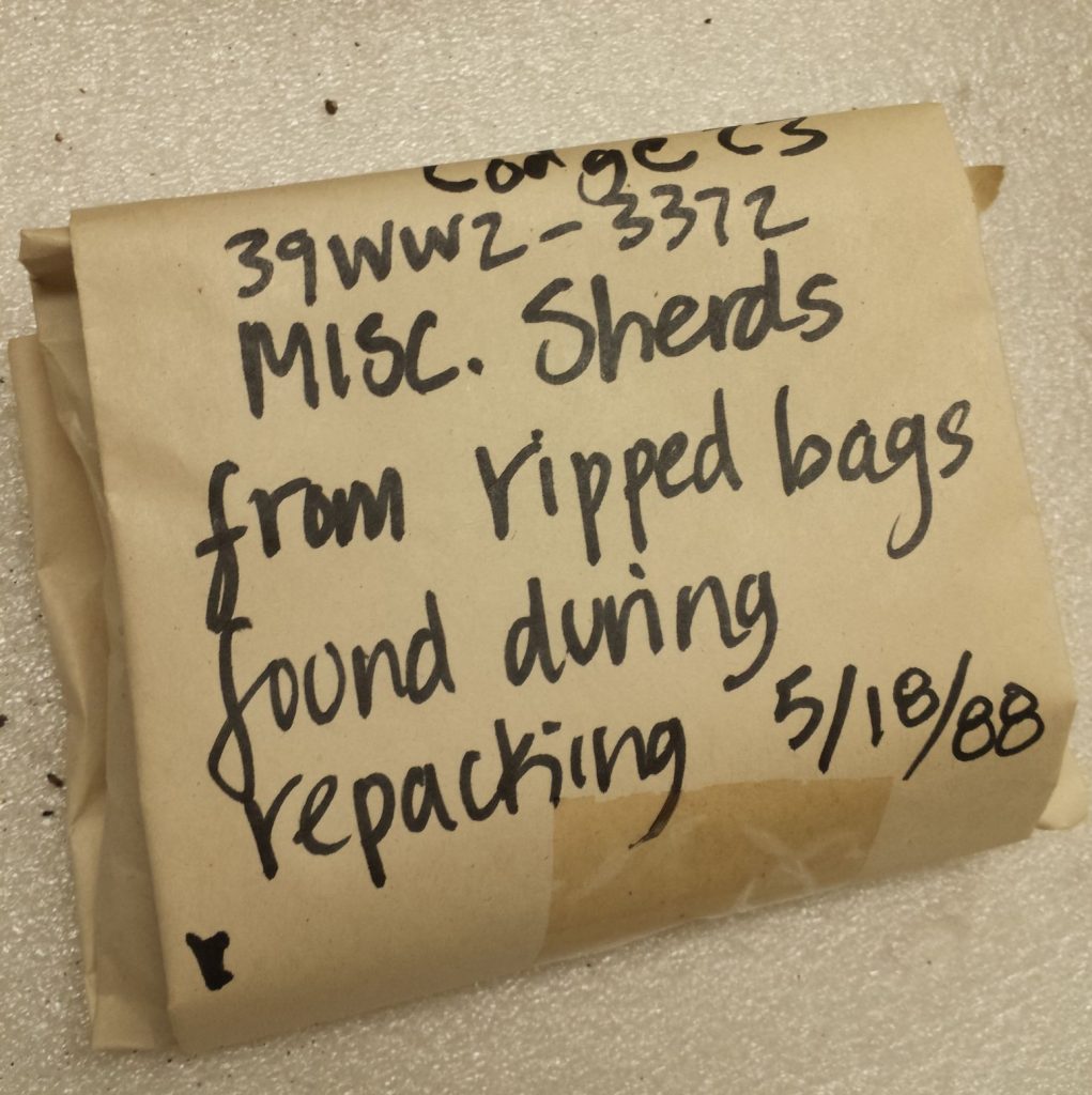 A paper bag with sharpie writing on it. Text reads "39ww2-3371 Misc. sherds from ripped bags found during repacking 5/18/88".