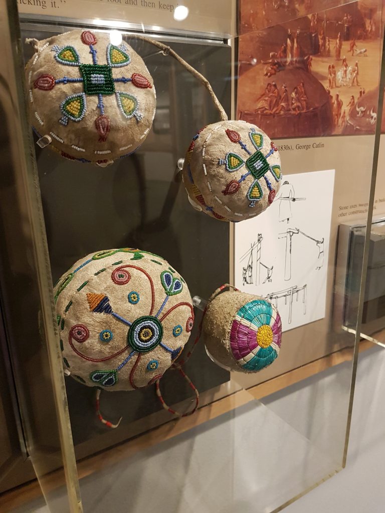 This display case contains small leather balls decorated with glass beads or porcupine quills. The designs are sort of abstract floral.