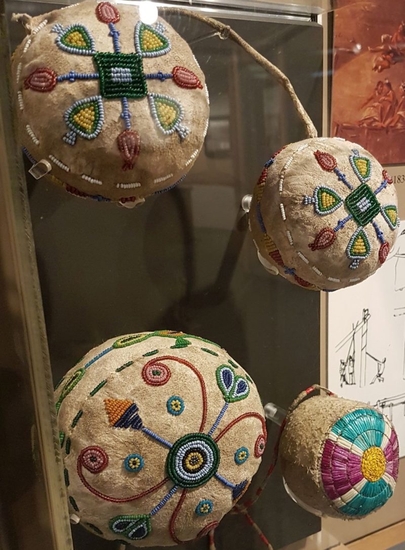 Display case containing small leather balls decorated with glass beads or porcupine quills. The designs are sort of abstract floral.