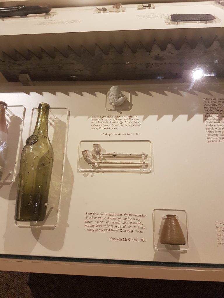 This display case holds glass bottles, clay pipes, and an ink well. Text by the pipes reads, "Engagees are giving a dance at their own expense in the dining room, which is near me. Meanwhile, I peels twigs of the upland willow and weave fancies over an occasional pipe of this Indian blend. Rudolph Friederich Kurz, 1851."
Text by the ink well reads, "I am alone in a smoky room, the thermometer 15 below zero, and although my ink is not frozen, my pen will neither move so nimbly, nor my ideas so freely as I could desire, when writing to my good friend Ramsey [Crooks]. Kenneth McKenzie, 1835."