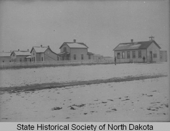 Old grainy photo of single- and two-story fort buildings in a snowy landscape.