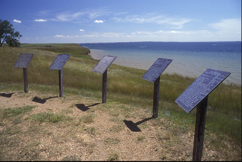 Five interpretive signs containing a lot of text, set up along the curved edge of a cleared area on a bluff overlooking the water.