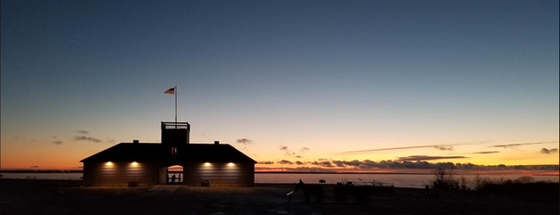 Wide landscape shot at sunset, showing the dark outline of the guardhouse against a darkening orange sky.