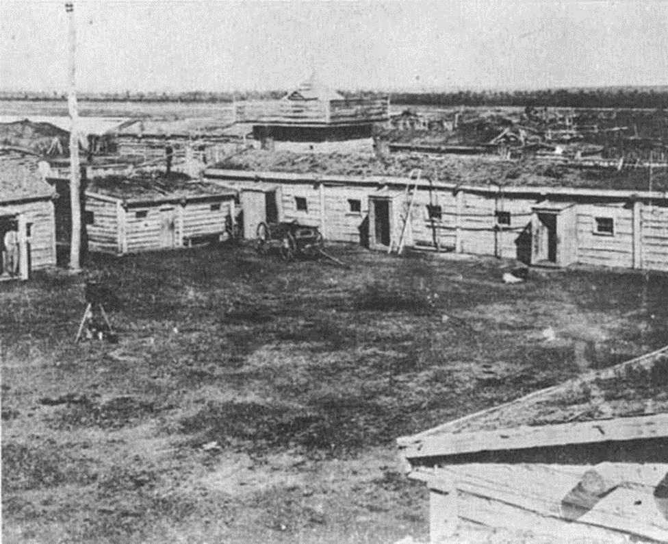 Black-and-white photo of the interior of the fort, showing an open space surrounded by log buildings.