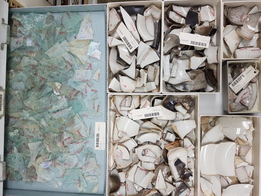 A storage drawer containing windowglass and stoneware sherds.