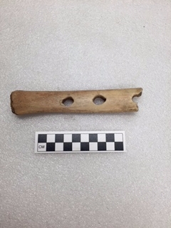 A partial bison rib bone with holes drilled into it.