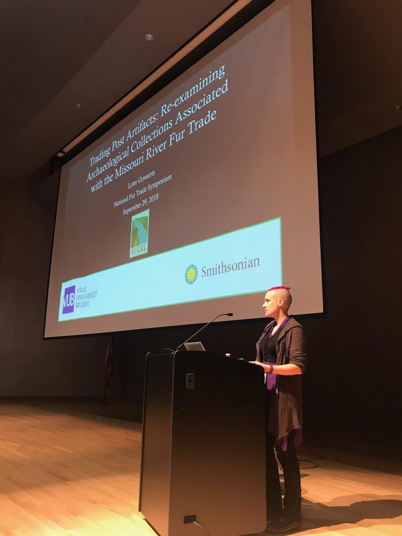 The author, standing at a lectern with the start slide of a presentation on a large screen behind.