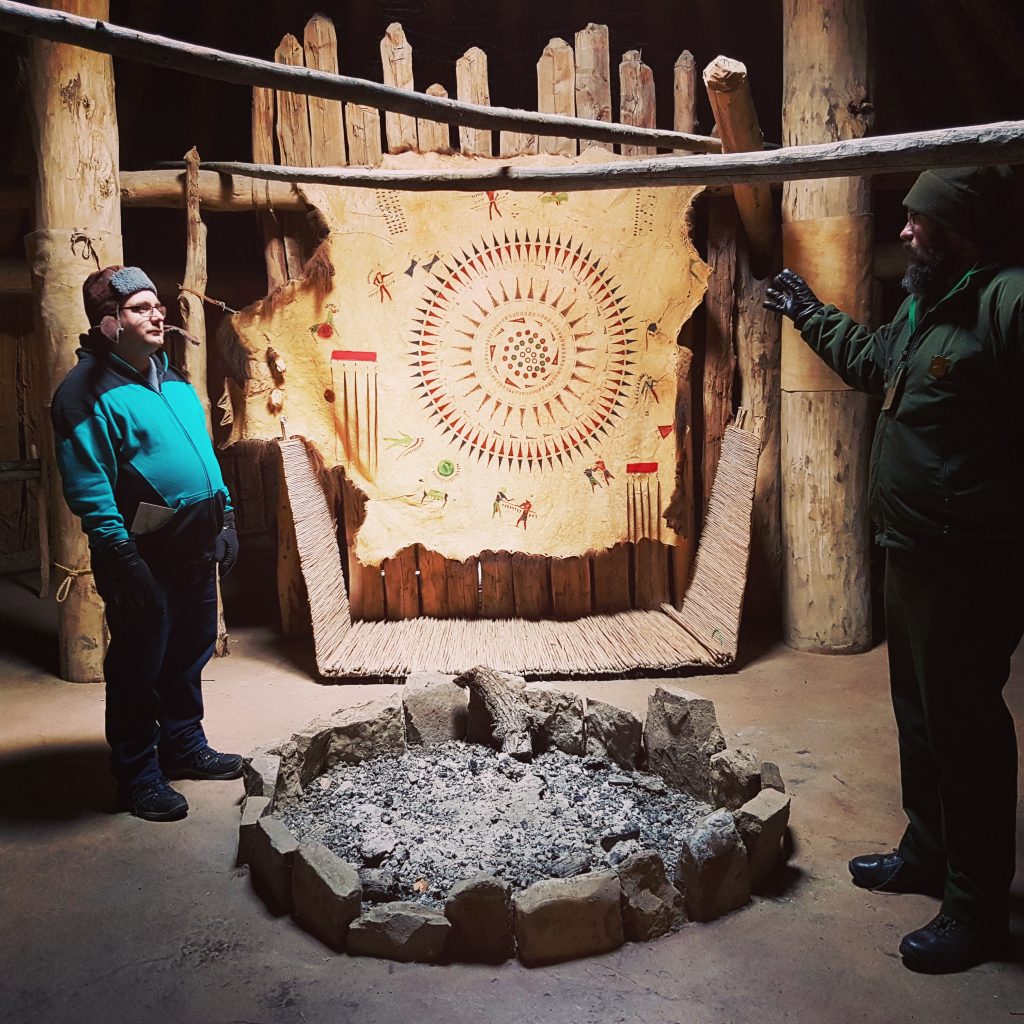My friend Mat and a park ranger standing inside the earth lodge, on opposite sides of the central hearth. Hanging up behind them is a decorated bison skin.