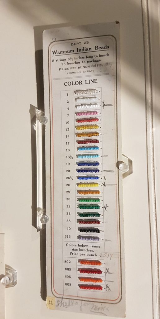 A cardboard sheet with many rows of sample beads. The sheet has holes punched in it, so bits of string with about a dozen of each color bead are attached to it.