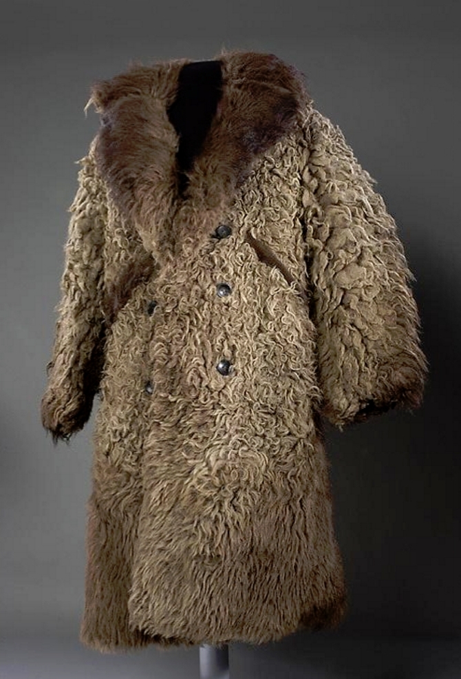 Color photo of a big fur coat on a stand. It has a large furry collar and double buttons going down the front.