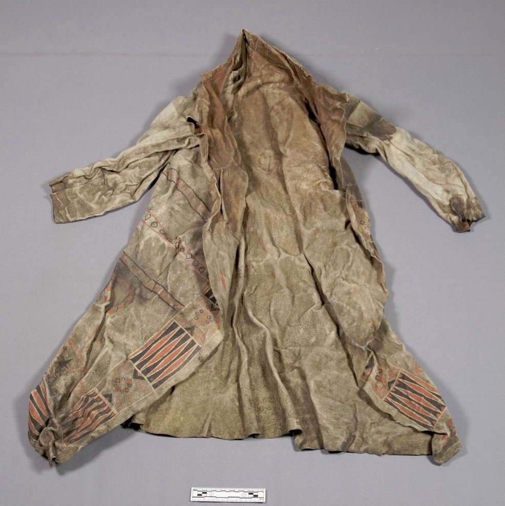 Color photo of a bison hide coat, laid out on a flat surface. It is decorated with orange and black lines and shapes.