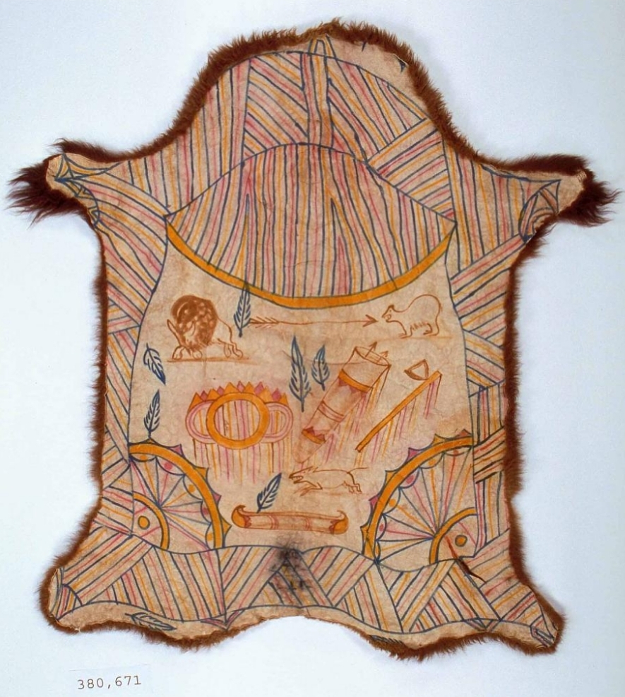 Color photo of a painted buffalo skin, laid out on a flat surface. It is decorated with lots of lines in black, orange, red, and yellow. In the center are depictions of animals and leaves.