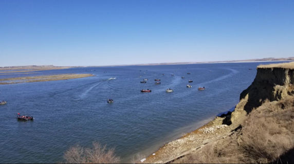 Color photo of a multitude of small fishing boats on the water of Lake Oahe. Blue sky overhead.