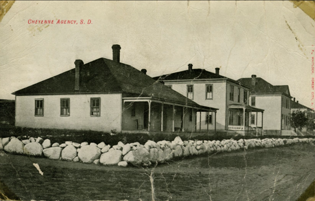 Postcard of black-and-white photo of three wooden frame buildings along a street. The words "Cheyenne Agency, S.D." are printed in red letters in the top left.