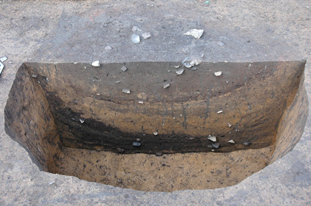 Another half excavated feature, this one photographed from the other side, so the profile wall is visible. Several different soil levels of different colors can be seen.